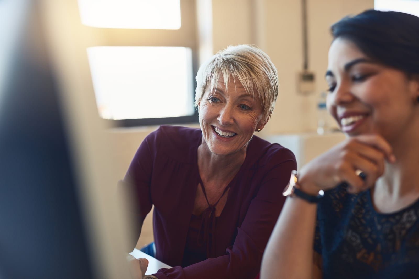 Support team member smiling while helping a colleague at a computer