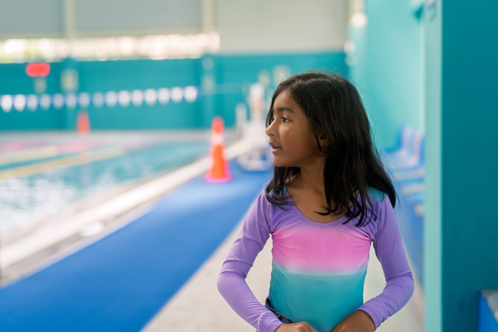 Young swimmer standing beside an indoor pool with safety cones on the deck