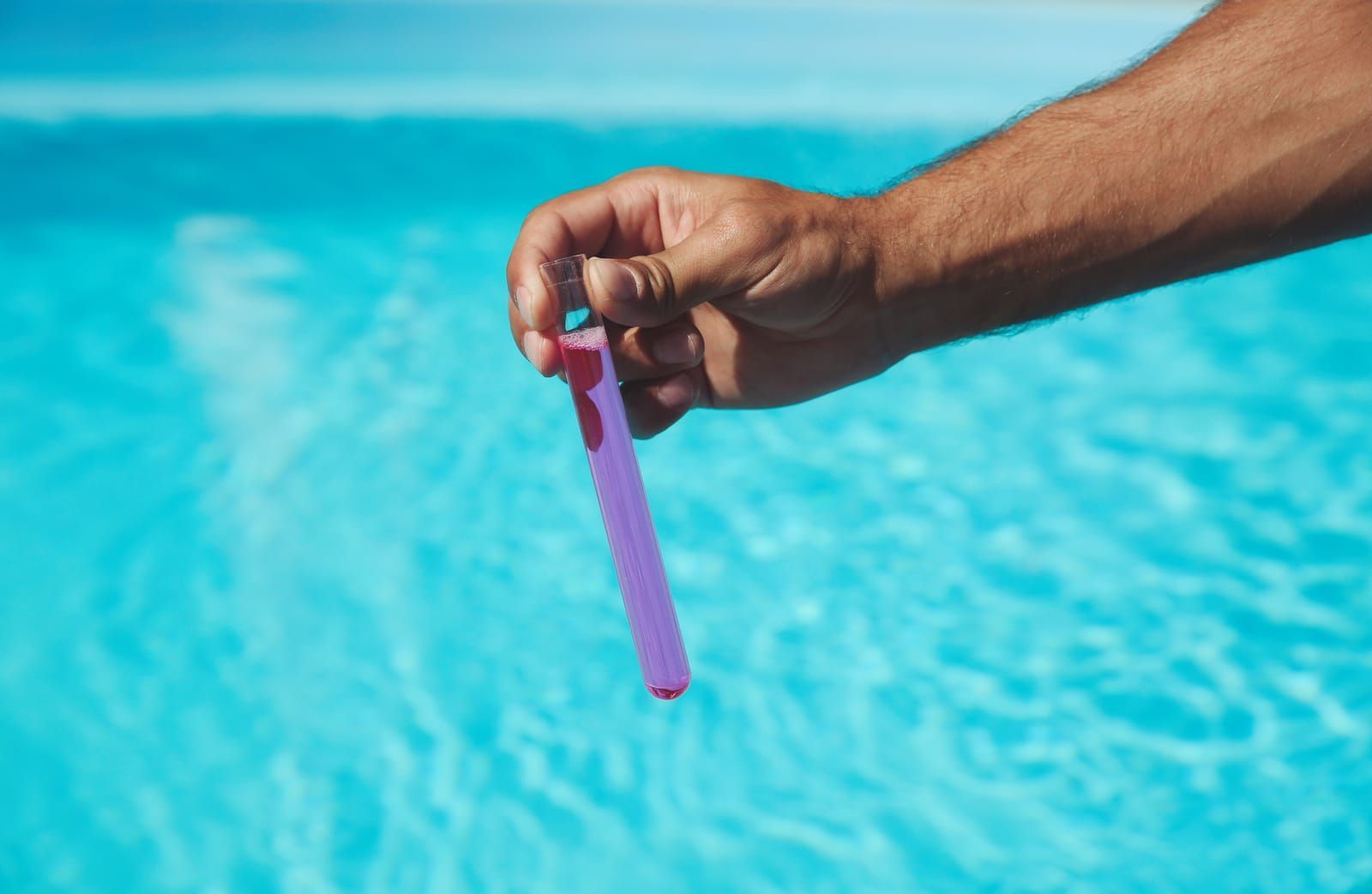 Hand holding a pool chemical test strip over clear blue water