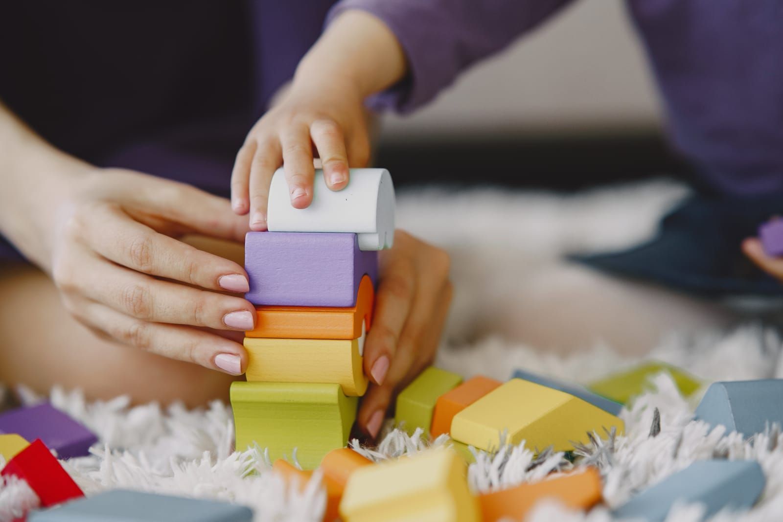 Adult and toddler stacking colorful wooden blocks together